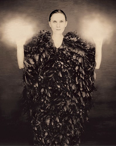 Joyce Tenneson, Self-Portrait with Lit Hands portrait of woman wearing a black feathered garment with glowing hands upraised